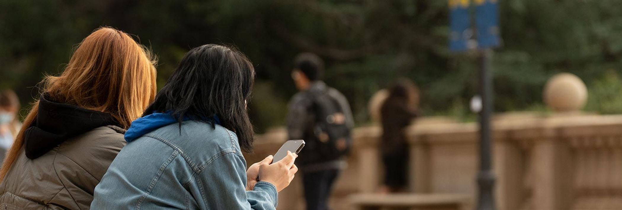 Three people sitting on a bench, two using phones, outdoors.